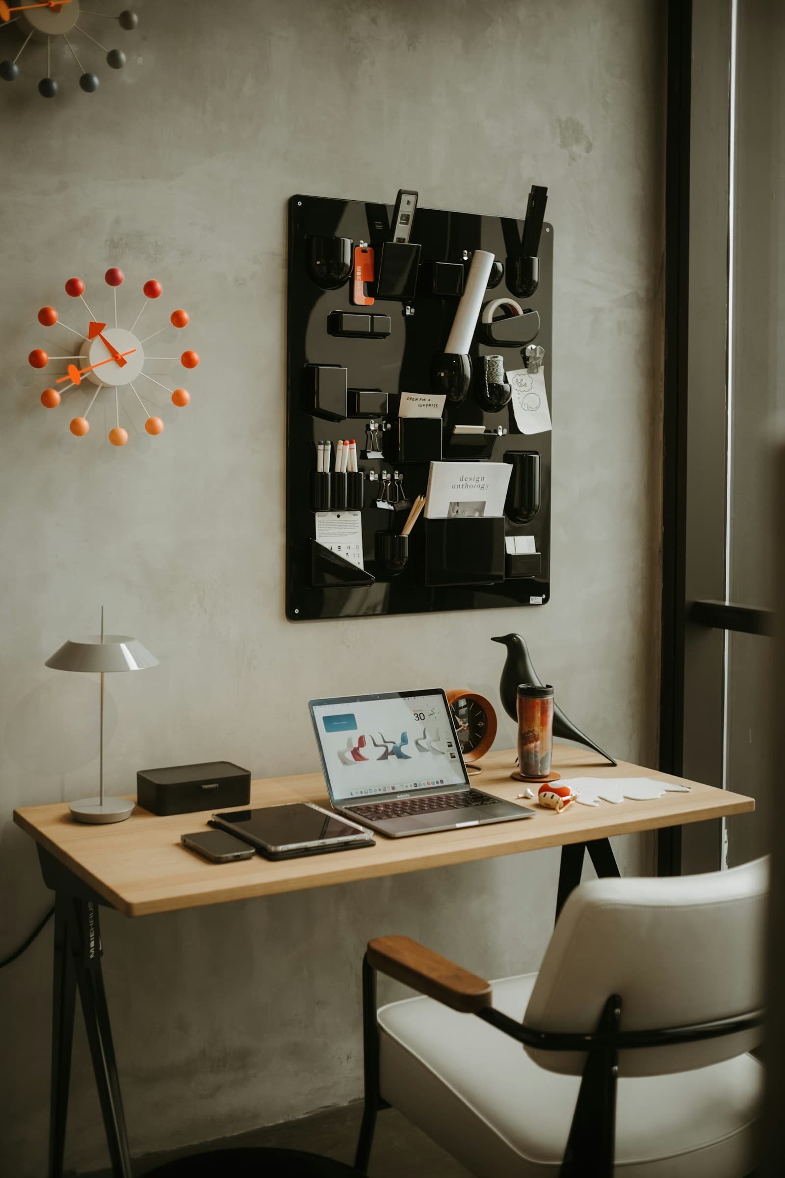 A warm design workspace with a laptop, wall organizer, and creative desk tools